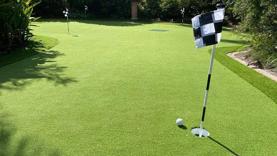 Synthetic turf All About Turf putting green with flag in backyard