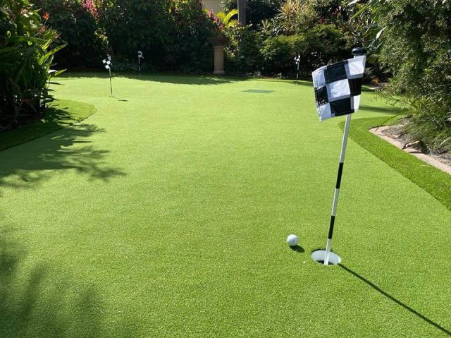 Synthetic turf All About Turf putting green with flag in backyard